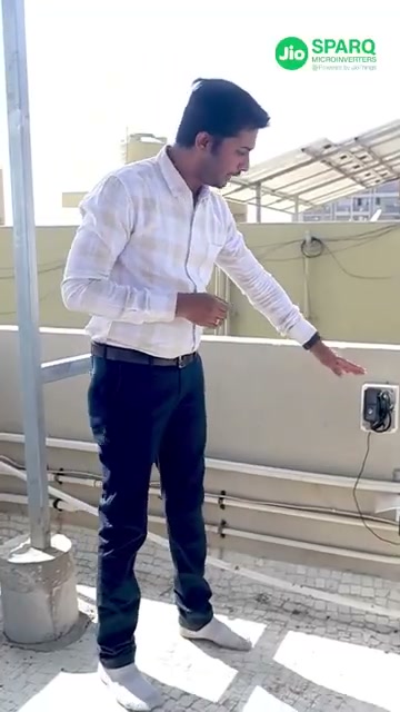 An installer on a roof terrace pointing at a small box mounted on the wall, a cable running from it